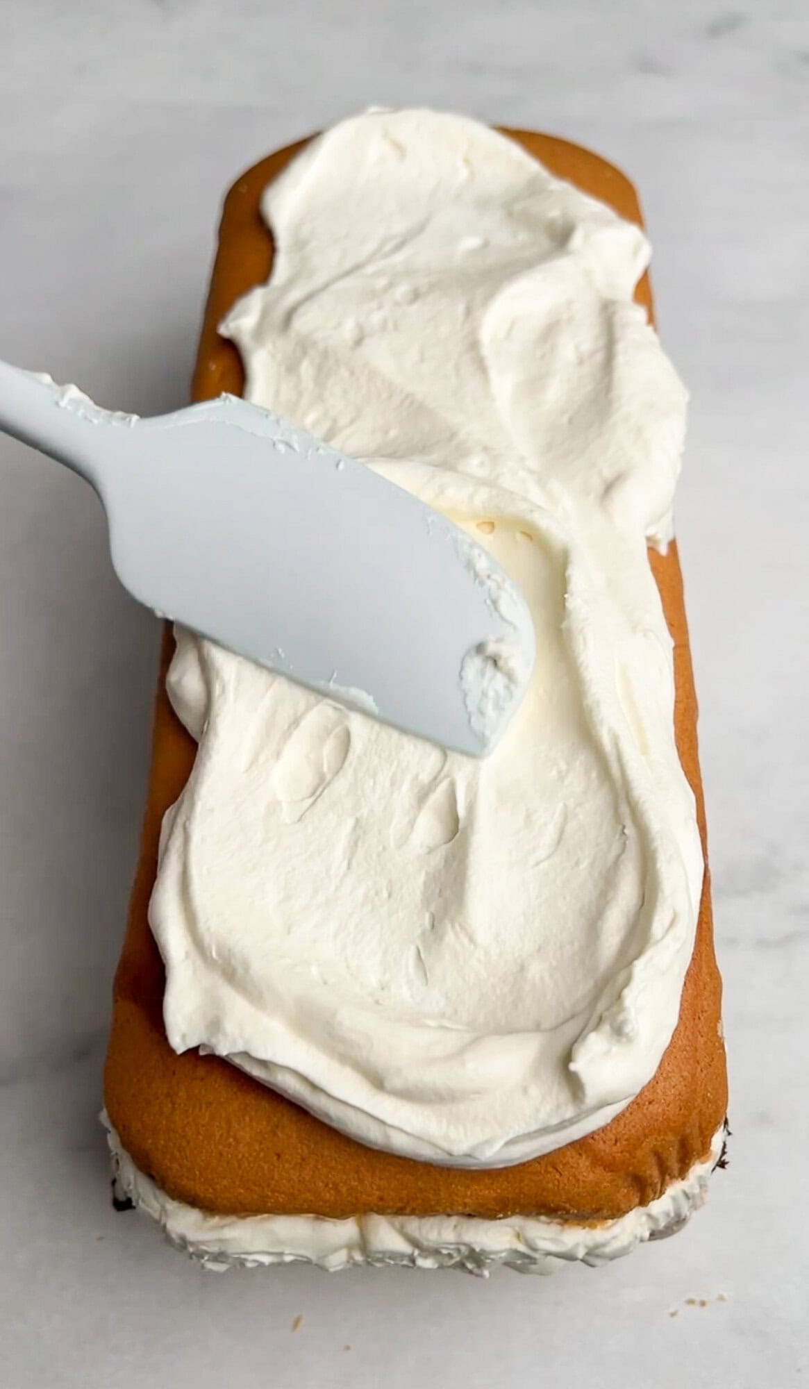 spreading whipped cream over the top layer ice cream cake