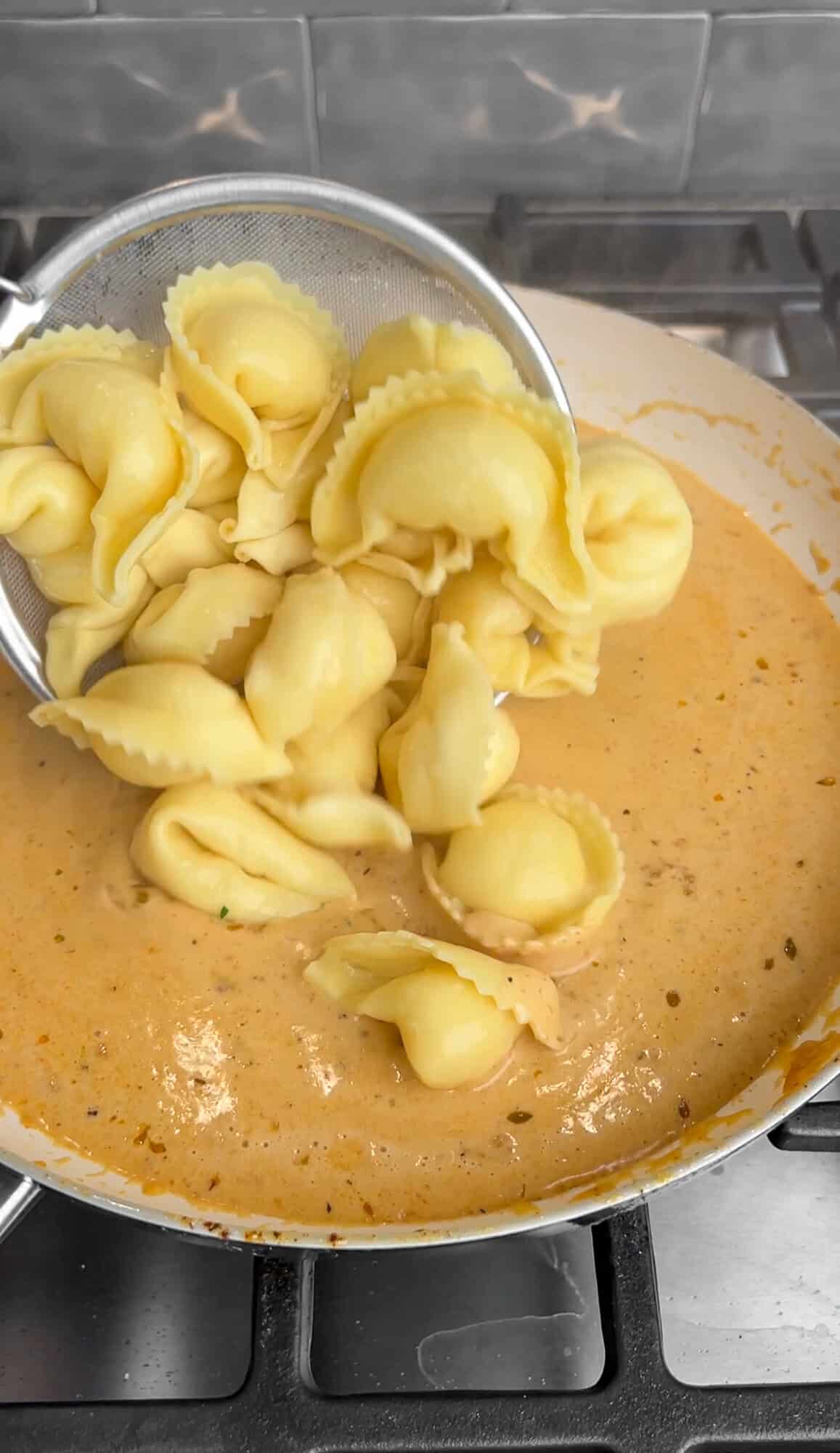 adding tortellini into creamy alfredo sauce
