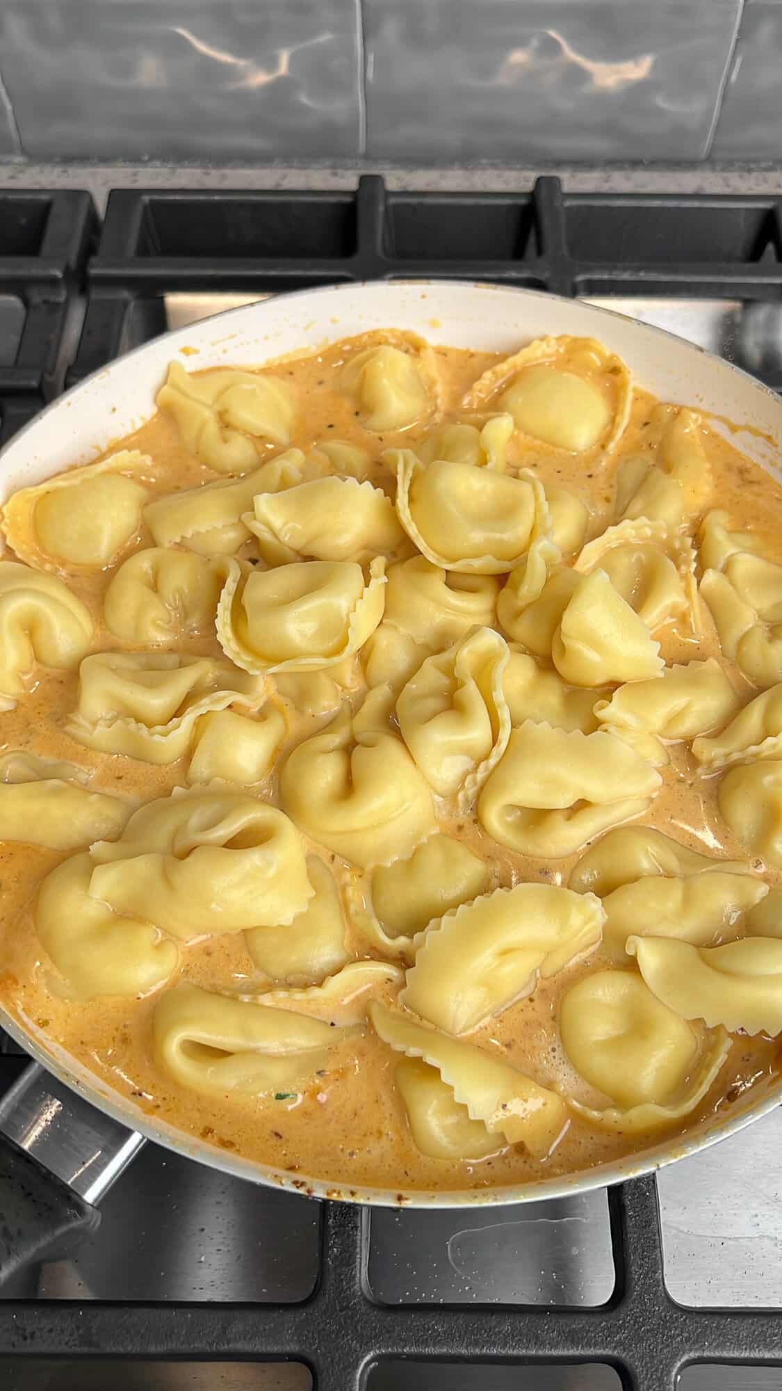 tortellini being added to the creamy alfredo sauce