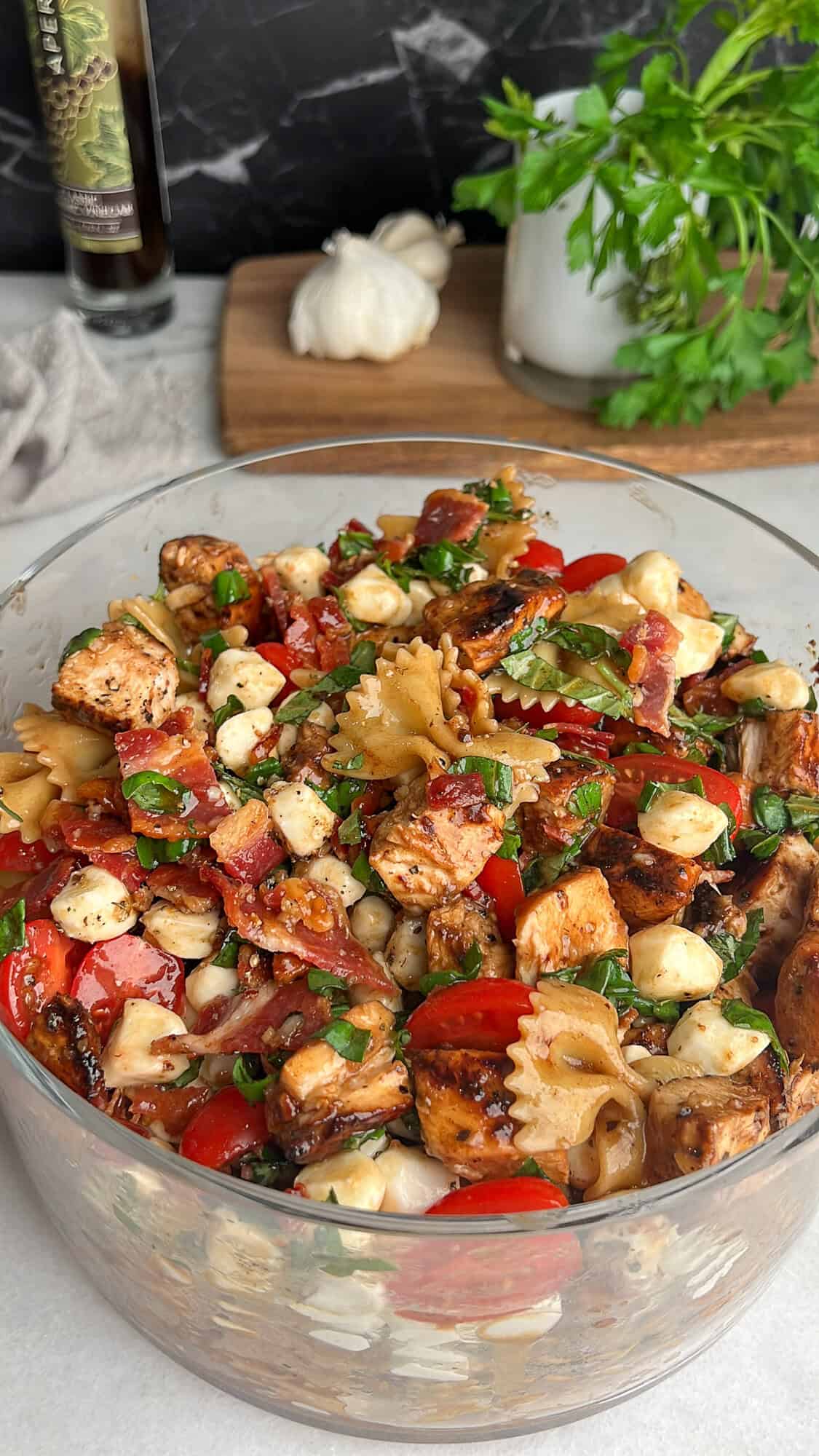 Caprese Pasta Salad is loaded with marinated chicken, tomatoes, mozzarella pearls, bacon, and basil tossed in a tangy balsamic dressing. Caprese pasta salad in a large glass bowl