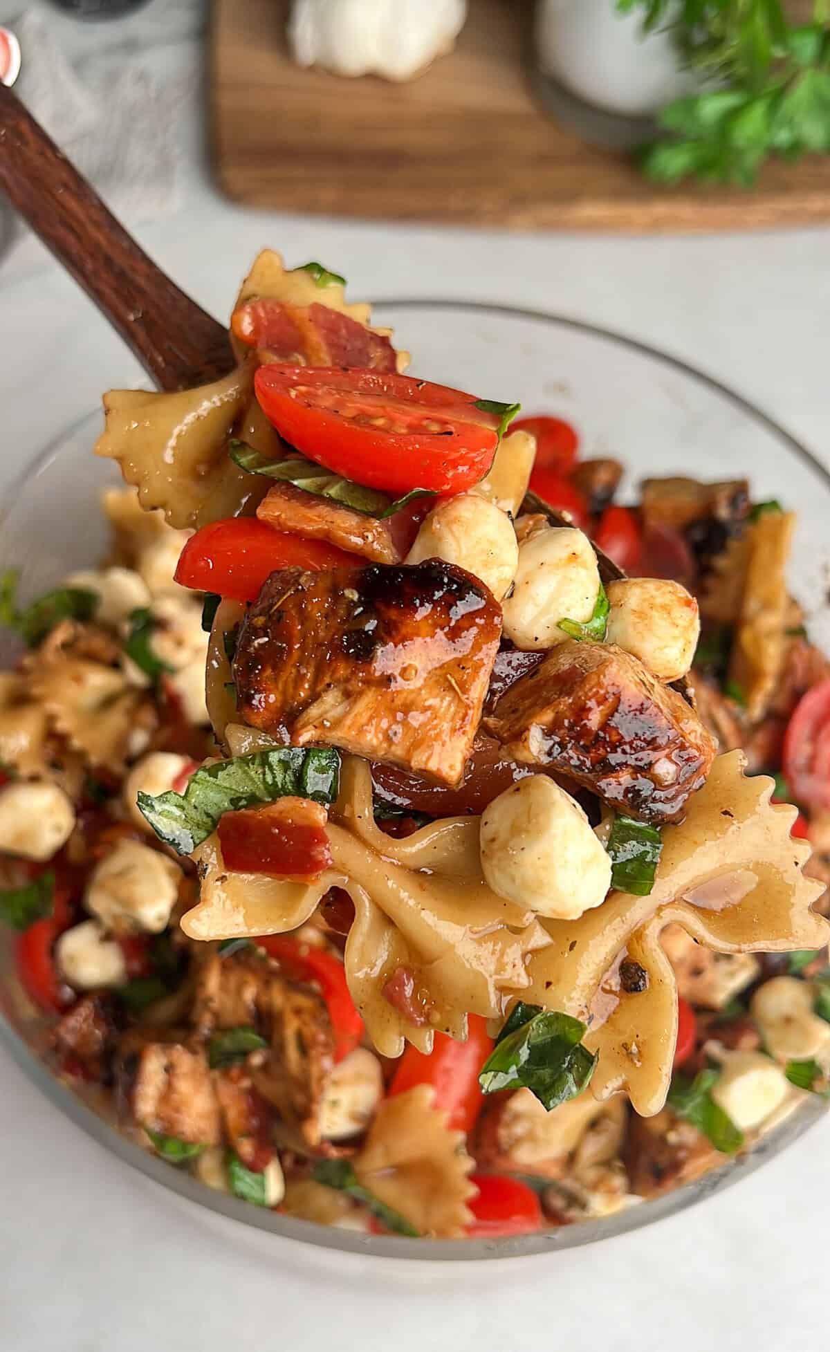 Caprese Pasta Salad is loaded with marinated chicken, tomatoes, mozzarella pearls, bacon, and basil tossed in a tangy balsamic dressing. A spoon serving caprese pasta salad