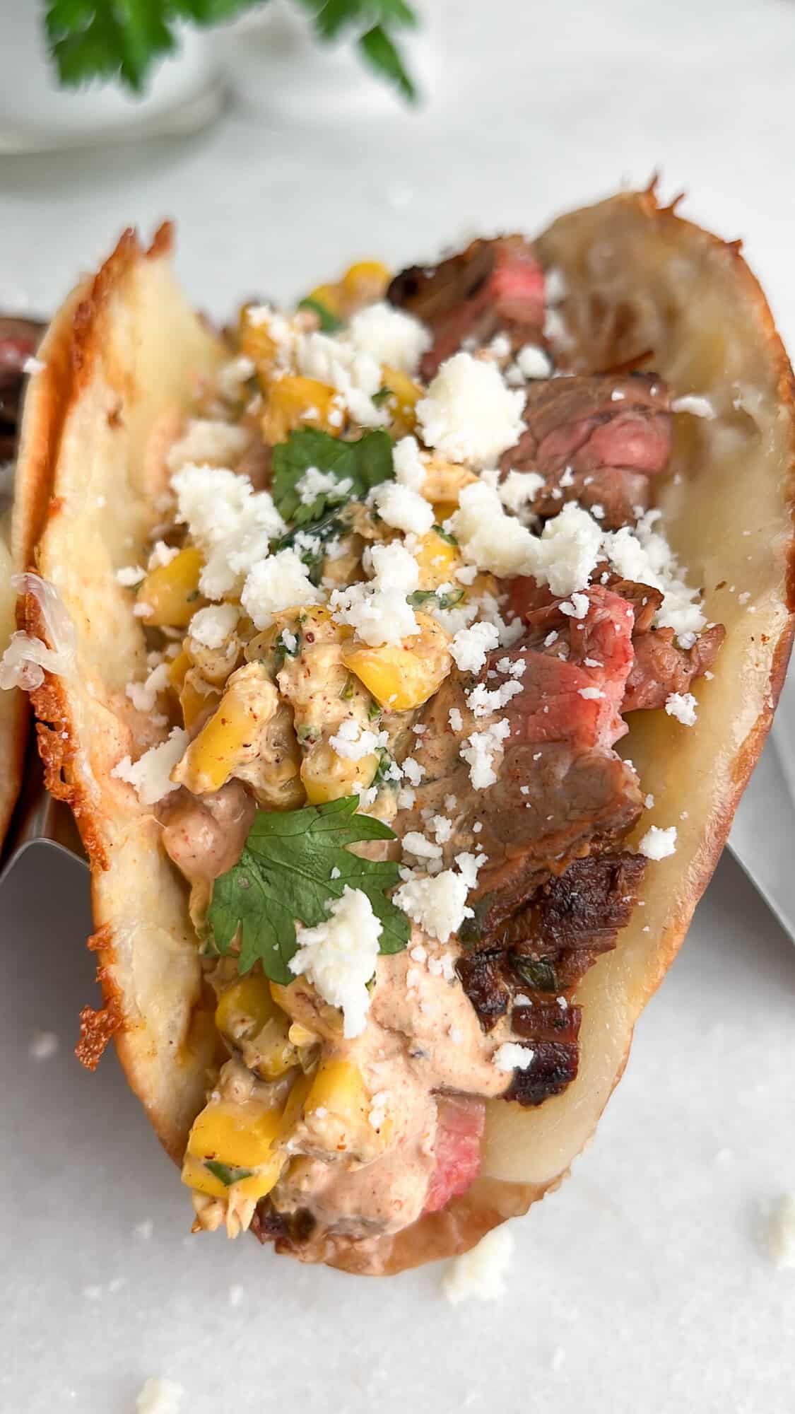 This Carne Asada Tacos recipe features juicy, citrus-marinated flank steak topped with street corn salad in cheesy tortillas. A carne asada taco with street corn salad in a taco holder