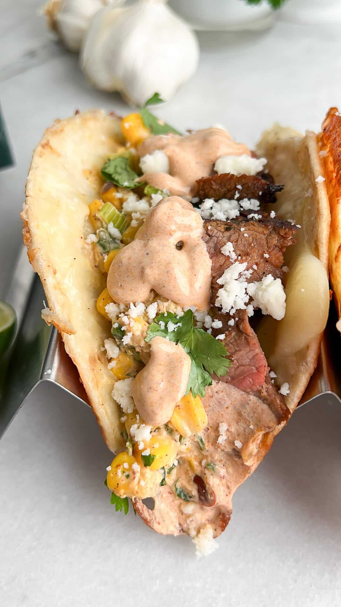 This Carne Asada Tacos recipe features juicy, citrus-marinated flank steak topped with street corn salad in cheesy tortillas. A carne asada taco with street corn and chipotle crema