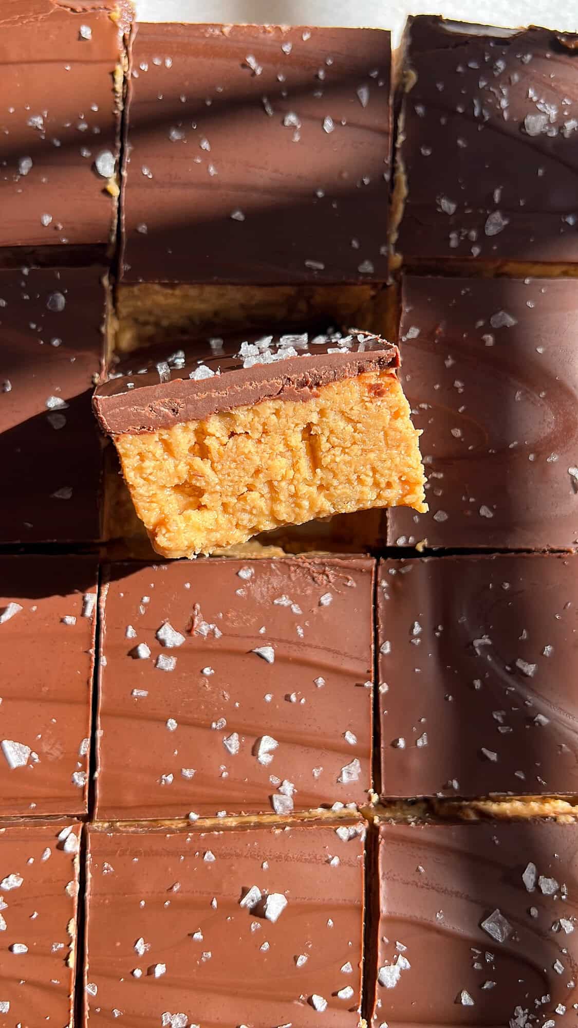 These no-bake peanut butter bars have a soft, sweet peanut butter base and a rich chocolate top with a sprinkle of flaky salt. Overhead view of no bake peanut butter bars, one on its side to show the layers