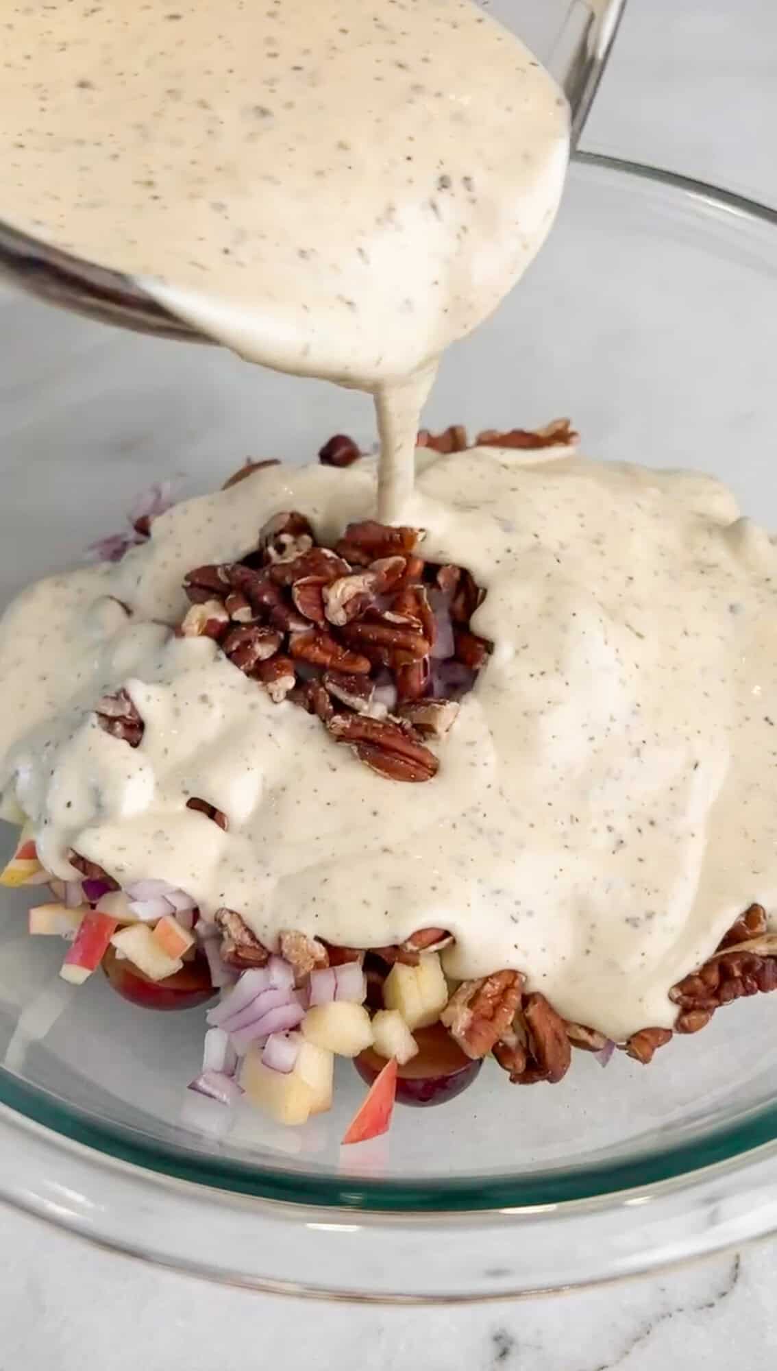 Tart grapes and apples, crunchy celery, red onion, pecans, and chicken are tossed in a creamy lemon dressing in this Waldorf Chicken Salad. Pouring lemon dressing over Waldorf salad ingredients