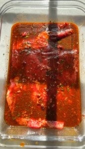 This Carne Asada Tacos recipe features juicy, citrus-marinated flank steak topped with street corn salad in cheesy tortillas. Flank steak marinating in a baking dish