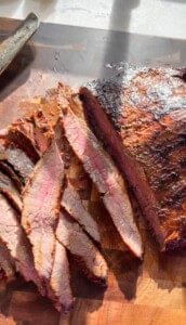 This Carne Asada Tacos recipe features juicy, citrus-marinated flank steak topped with street corn salad in cheesy tortillas. Sliced carne asada on a cutting board