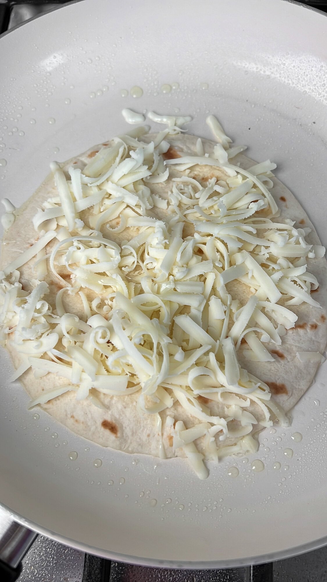 This Carne Asada Tacos recipe features juicy, citrus-marinated flank steak topped with street corn salad in cheesy tortillas. A tortilla topped with shredded Oaxaca cheese in a pan