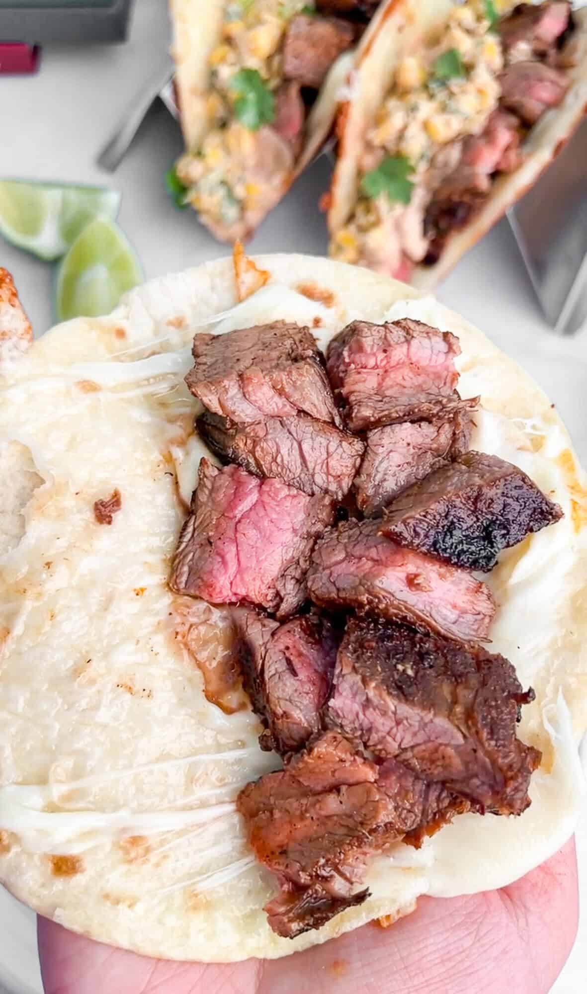 This Carne Asada Tacos recipe features juicy, citrus-marinated flank steak topped with street corn salad in cheesy tortillas. Pieces of carne asada on a cheesy toasted tortilla