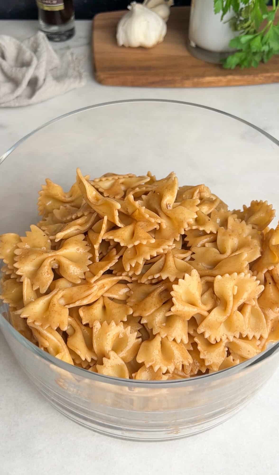 Caprese Pasta Salad is loaded with marinated chicken, tomatoes, mozzarella pearls, bacon, and basil tossed in a tangy balsamic dressing. Bow tie noodles in a glass bowl