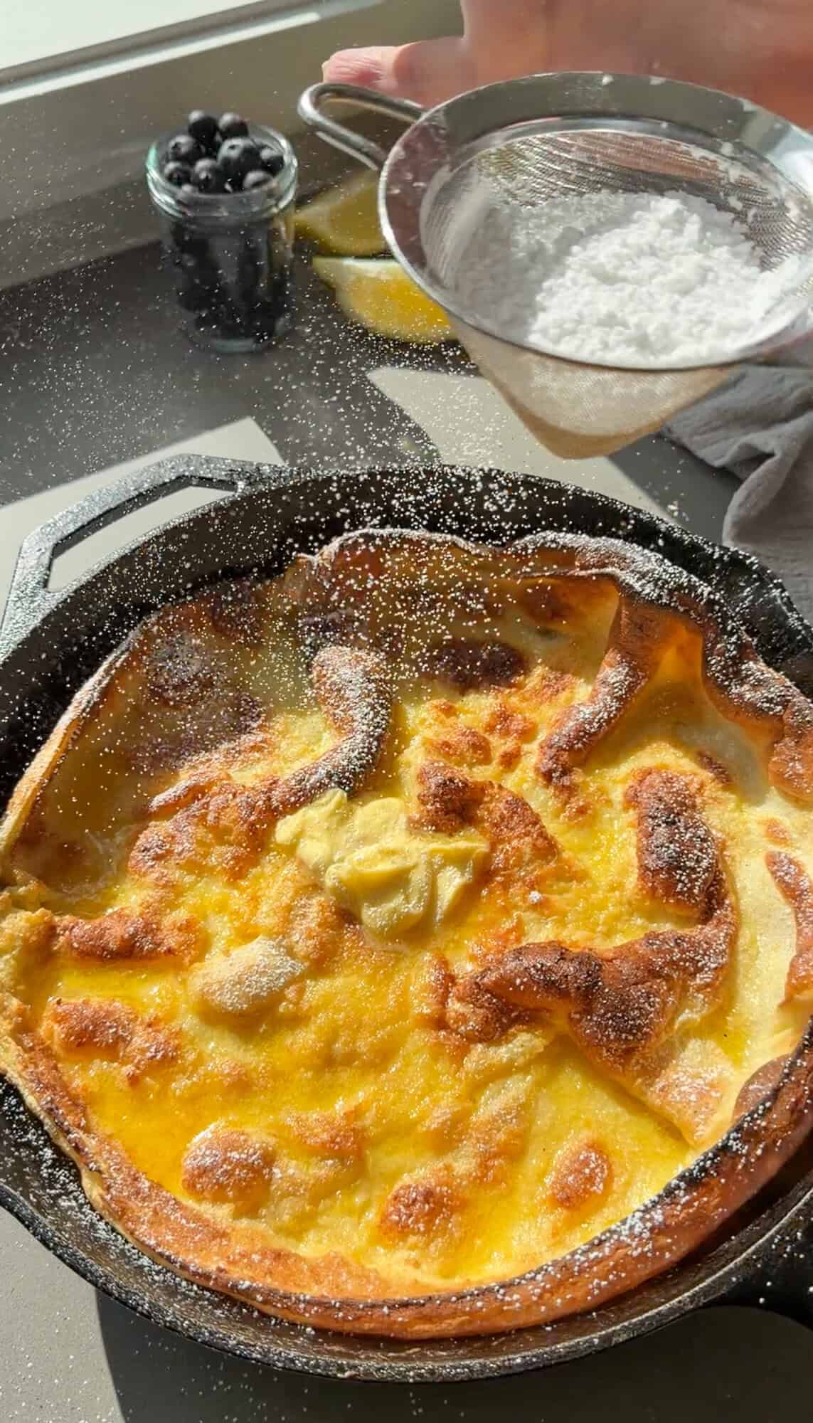 sifting powdered sugar over a dutch baby pancake