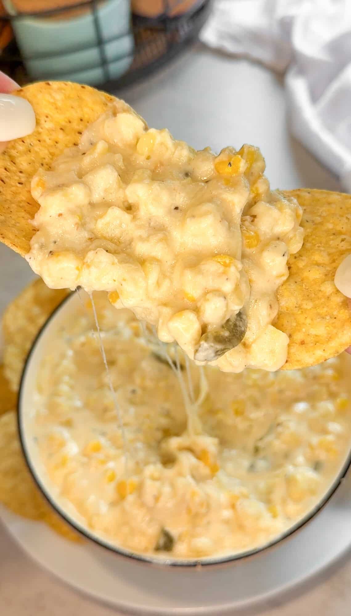 cheesy hot corn dip being scooped with tortilla chips