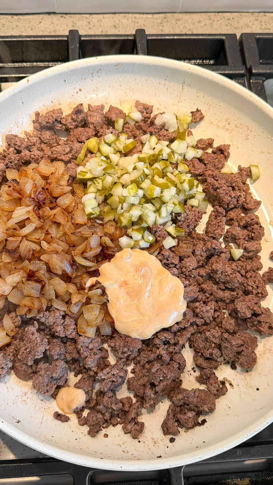 adding onions, pickles and burger sauce to ground hamburger
