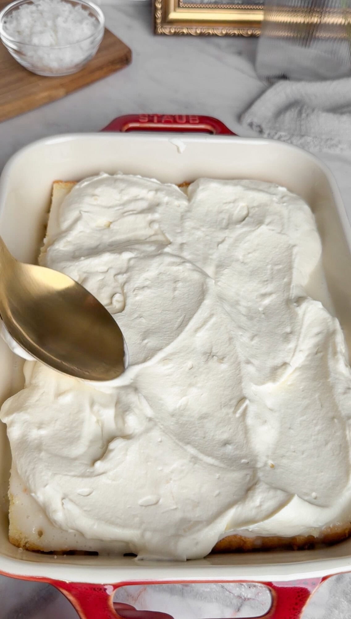 spreading whipped cream on coconut cake
