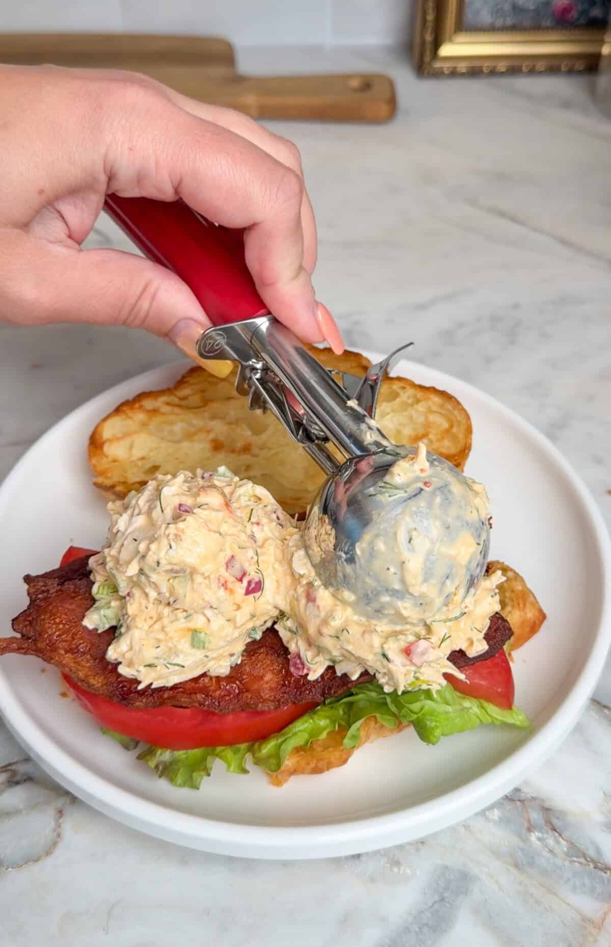 adding scoops of chicken salad to a croissant