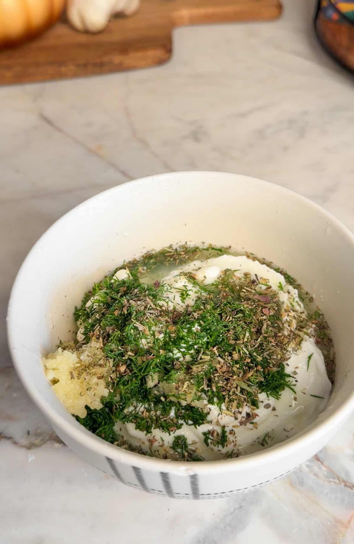 An easy Greek chicken rice bowl with juicy air-fryer chicken skewers, fresh tomato-cucumber salad and creamy garlic-dill yogurt sauce. Greek yogurt, mayo, fresh dill, garlic, lemon juice, salt, and pepper in a bowl.