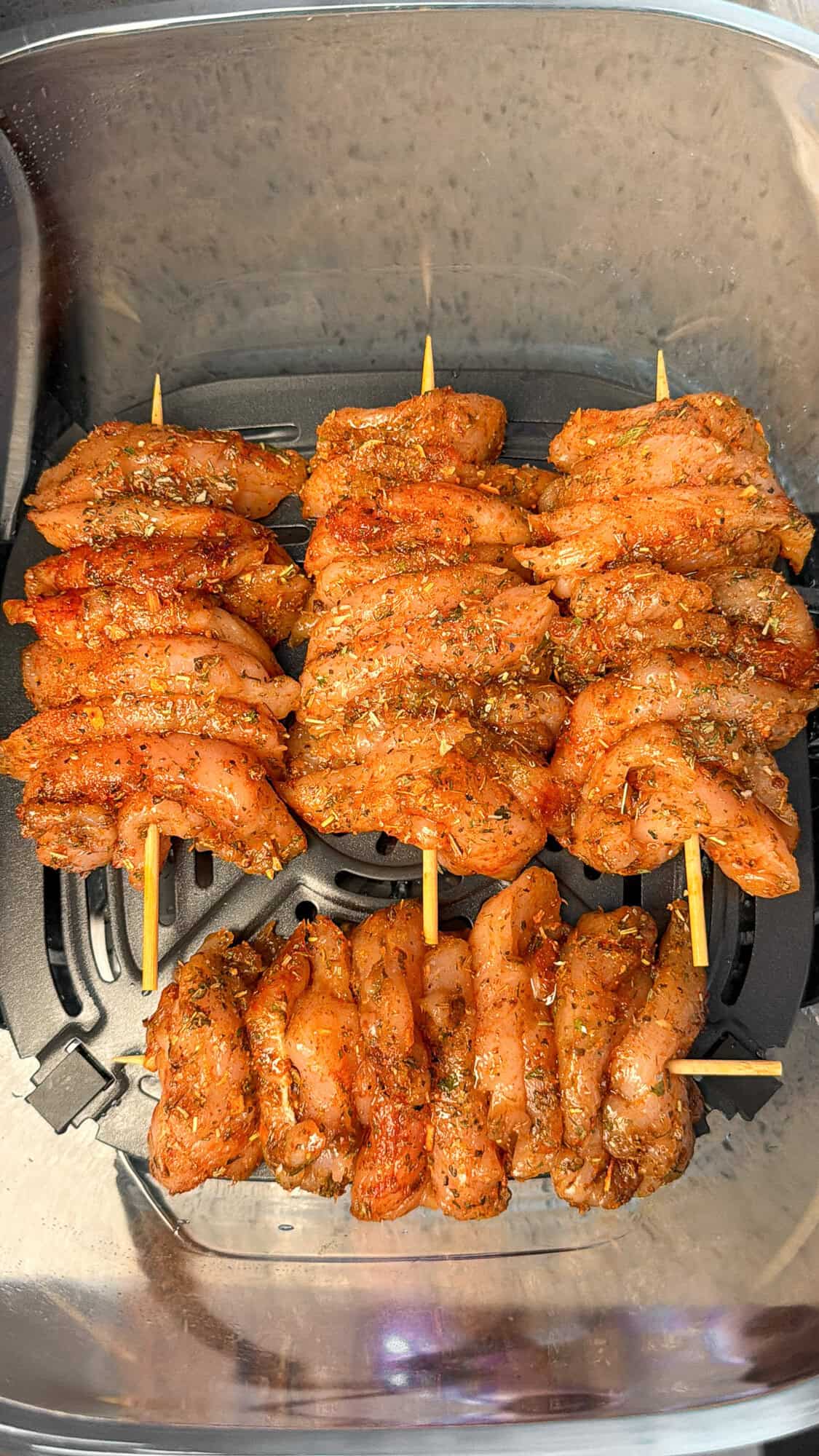 Season and Marinate the Chicken Greek marinated chicken skewers in the basket of an air fryer.