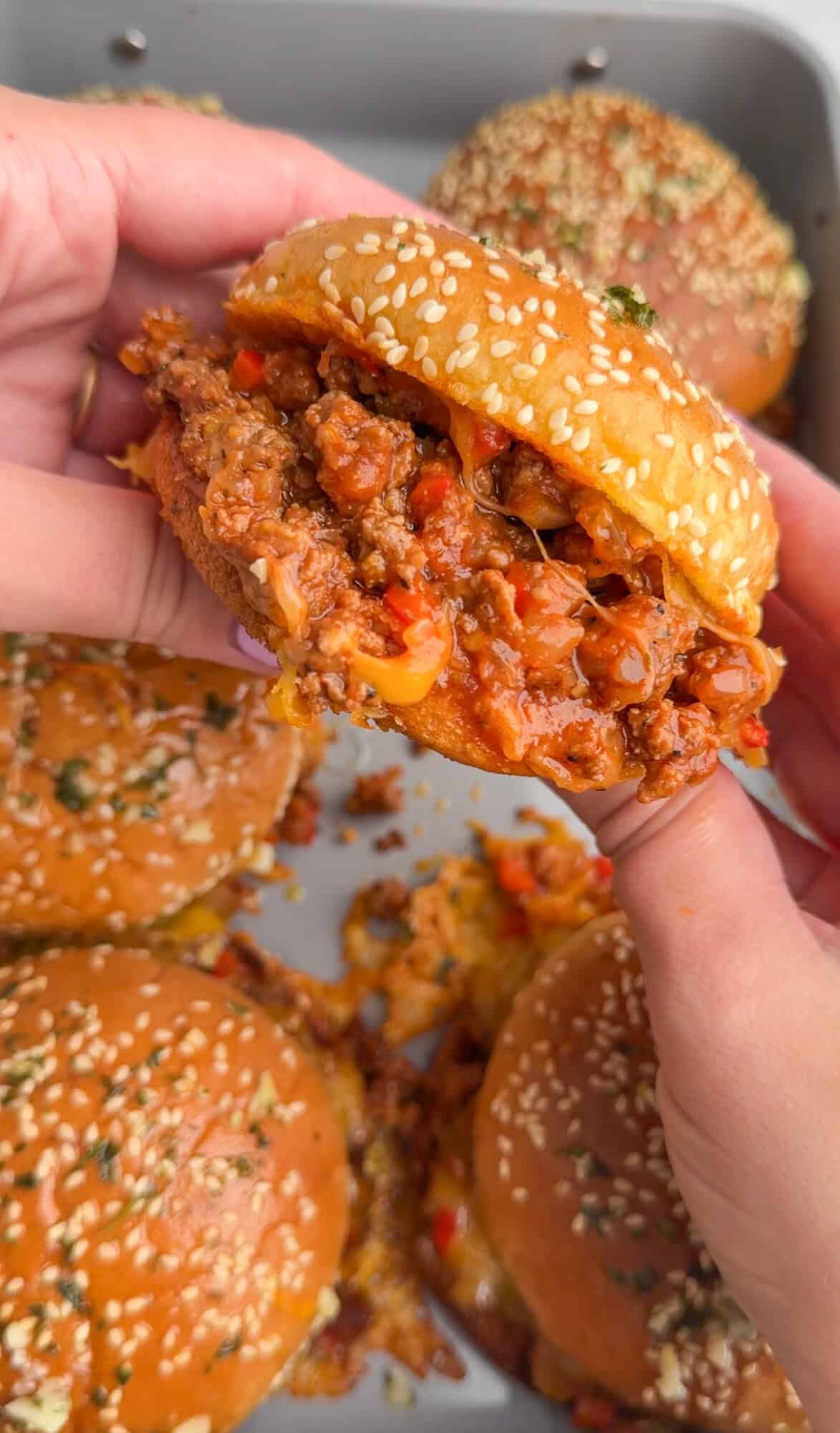 Hands holding a homemade sloppy Joe filled with beefy sauce and melted cheese.
