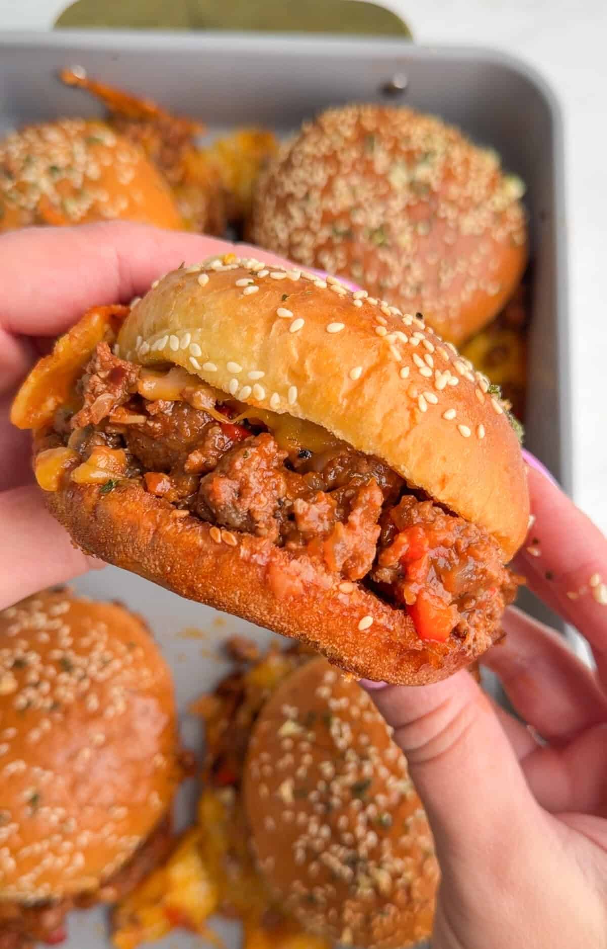 Hands holding a sloppy Joe filled with beefy sauce and melted cheese.
