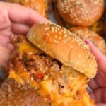 Hands holding a sloppy Joe over a baking dish fully of homemade sloppy Joes.