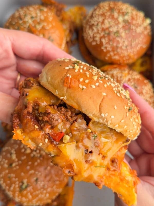 Hands holding a sloppy Joe over a baking dish fully of homemade sloppy Joes.