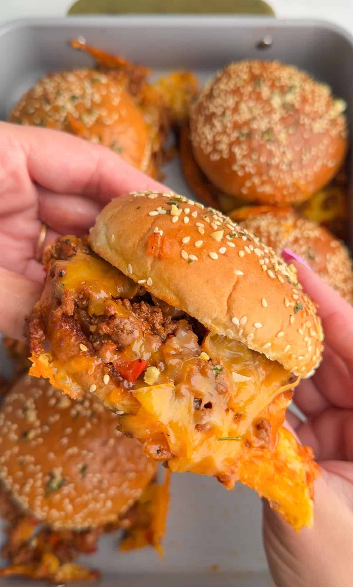 Hands holding a sloppy Joe over a baking dish fully of homemade sloppy Joes.