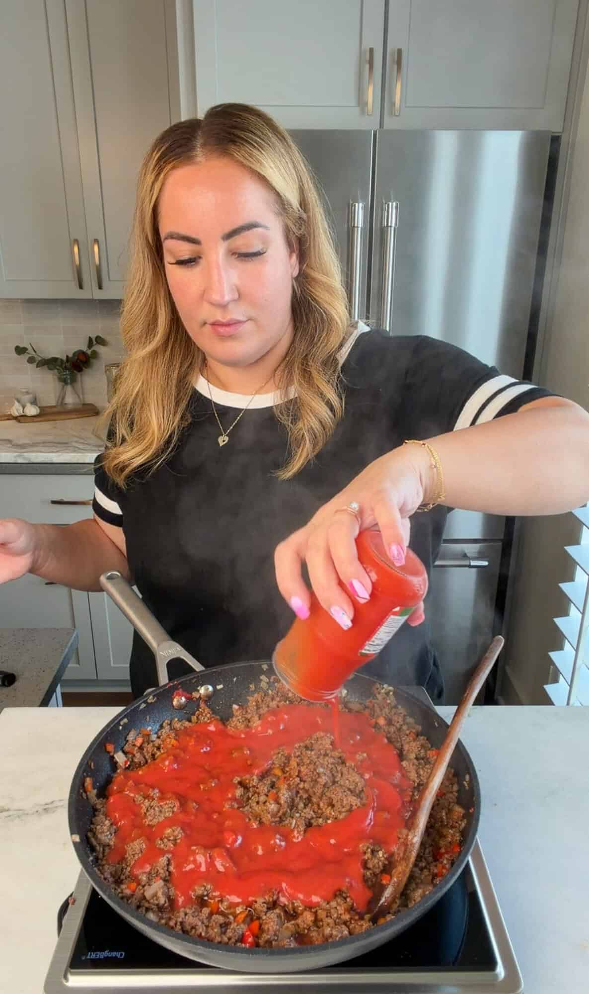 Adding passata to a skillet of homemade sloppy Joes filling.