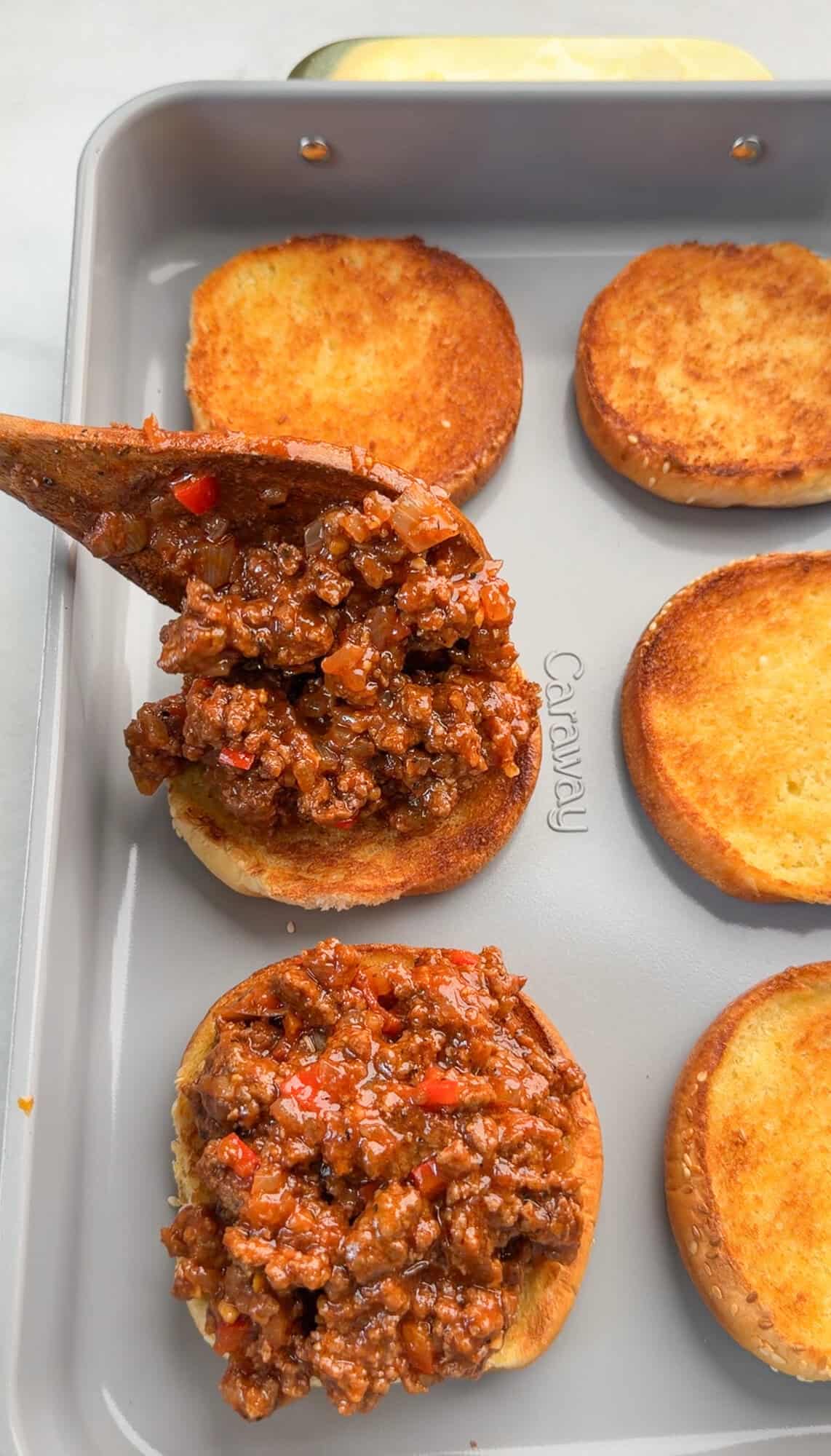 Spooning sloppy Joe filling over toasted buns.