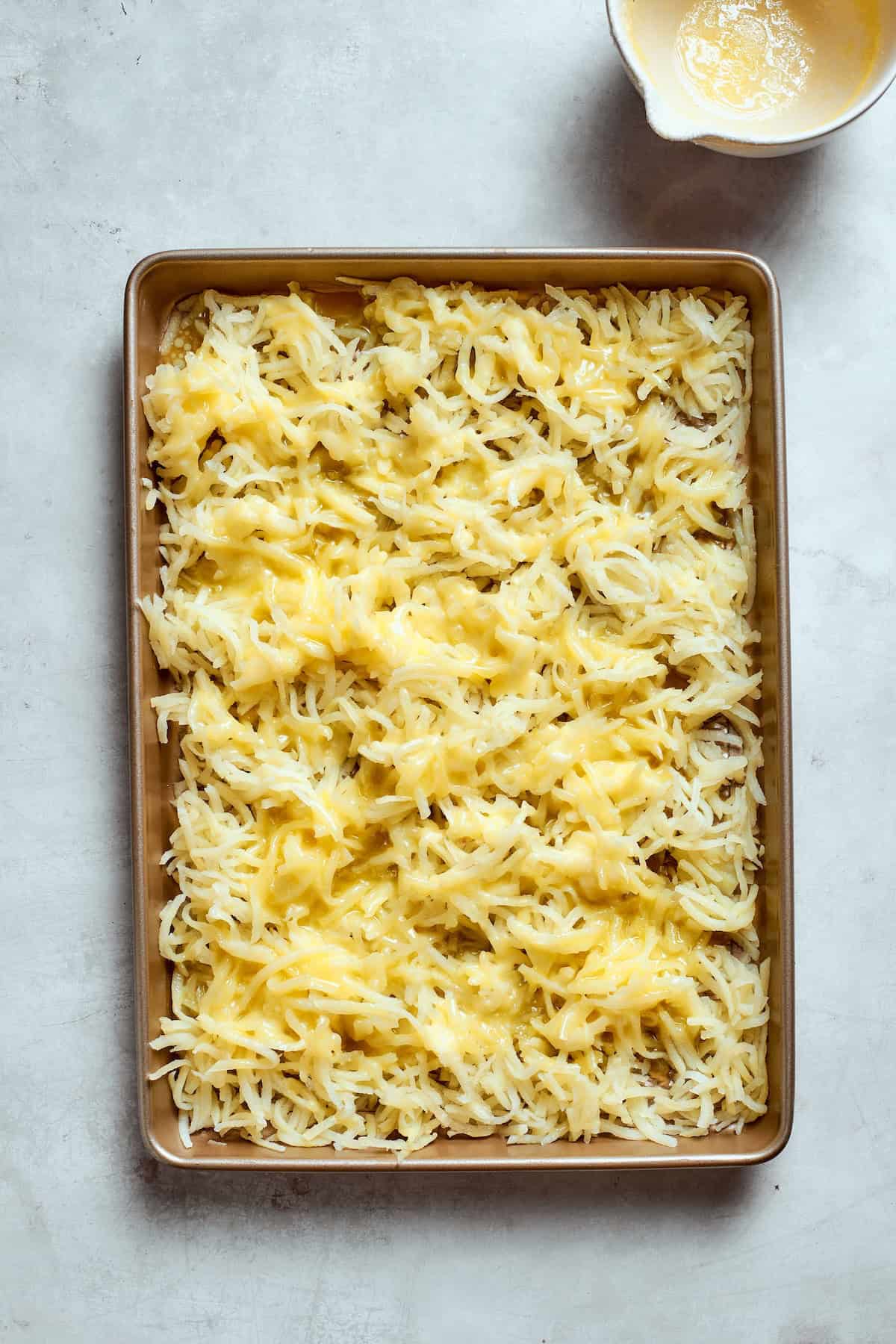 Loaded with bacon, eggs, and cheese and baked in one dish, this hashbrown breakfast casserole is the easiest way to do brunch for a crowd. Hashbrowns spread over a baking sheet and covered with melted butter.
