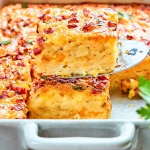 A spatula lifting a slice of hashbrown casserole from the baking dish.