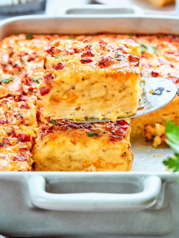 A spatula lifting a slice of hashbrown casserole from the baking dish.