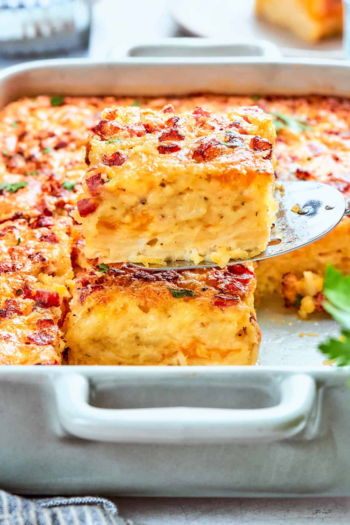 A spatula lifting a slice of hashbrown casserole from the baking dish.
