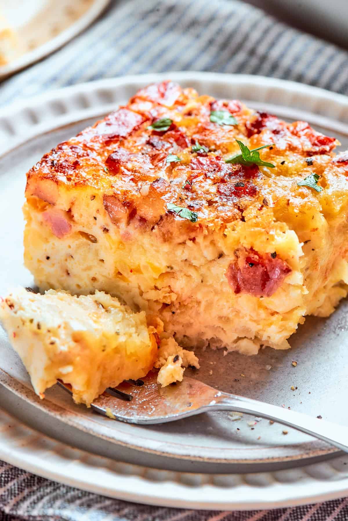 Loaded with bacon, eggs, and cheese and baked in one dish, this hashbrown breakfast casserole is the easiest way to do brunch for a crowd. Close-up of a slice of hashbrown breakfast casserole on a plate with a bite removed by a fork.
