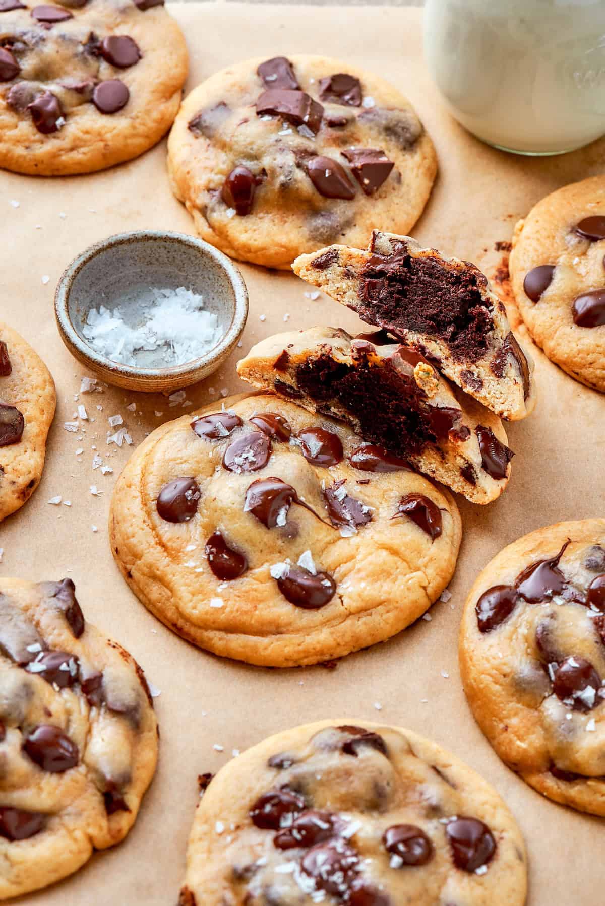 Double dessert? Yes! These brownie-stuffed cookies wrap gooey brownie bites in chewy, golden-brown chocolate chip cookies. Overhead of brownie stuffed chocolate chip cookies on parchment paper with one cut in half to reveal the inside.