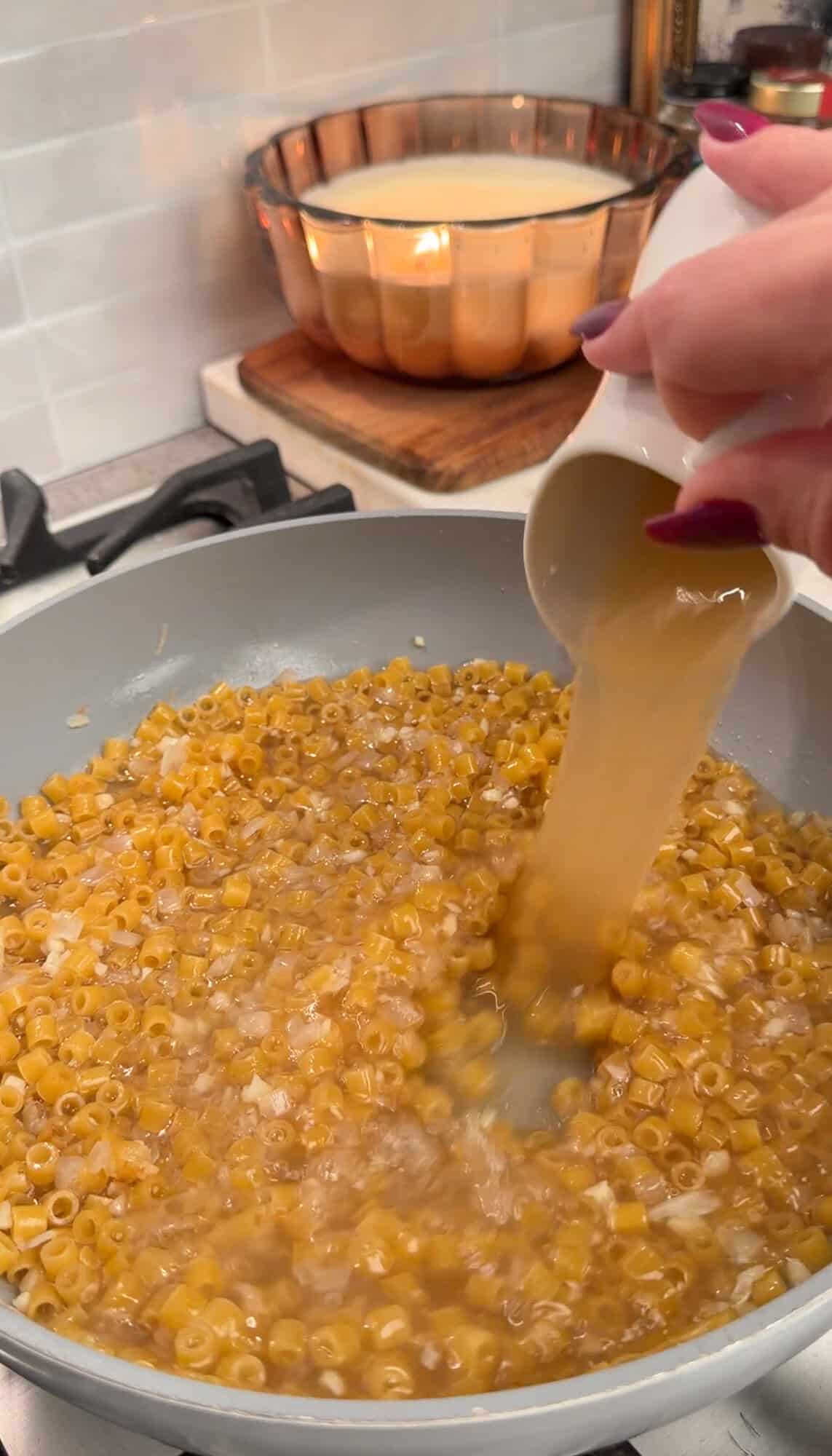 adding chicken stock in broccoli cheddar pasta in a pan